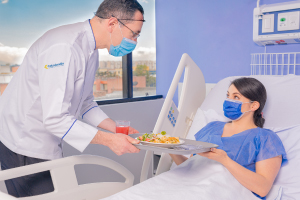 Enfermero lleva bandeja de comida a mujer que está en camilla hospitalaria