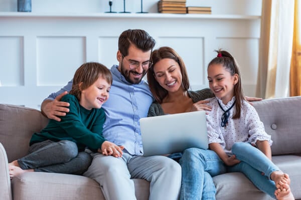 Familia feliz observando en su computador portátil los beneficios que brinda Colsubsidio.