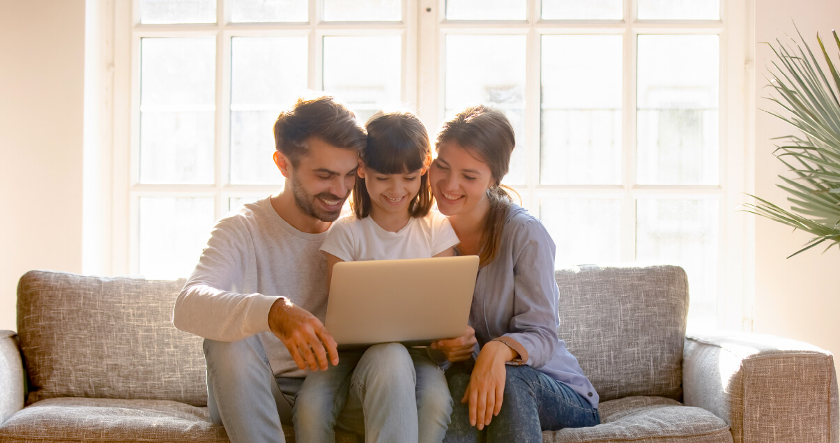 Papá, hija y mamá están en la sala de su casa navegando la página de diversión Colsubsidio para inscribirse a los programas presenciales y virtuales. 
