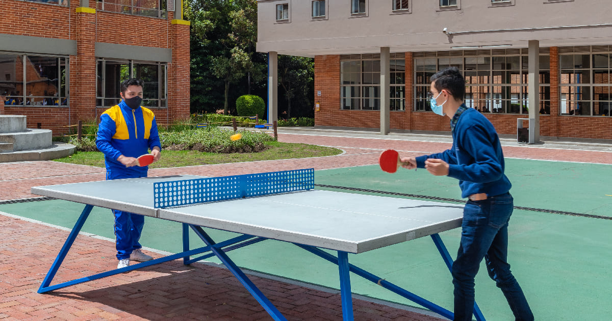 Dos estudiantes de los Colegios Colsubsidio jugando ping pong, al aire libre, en las instalaciones de la institución educativa. 